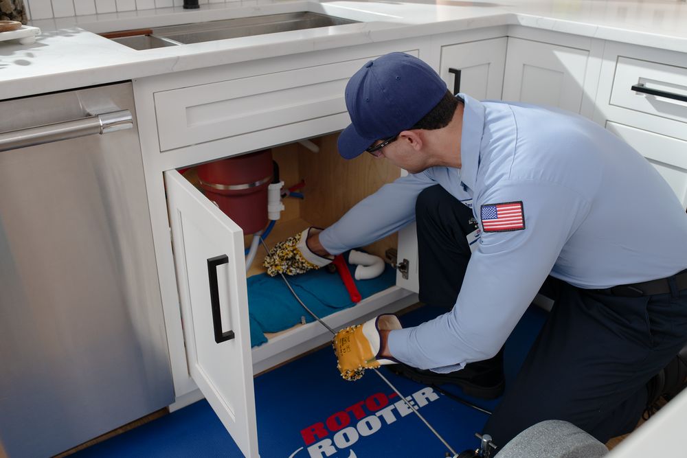 Roto-Rooter plumber running a drain cable through a kitchen sink line